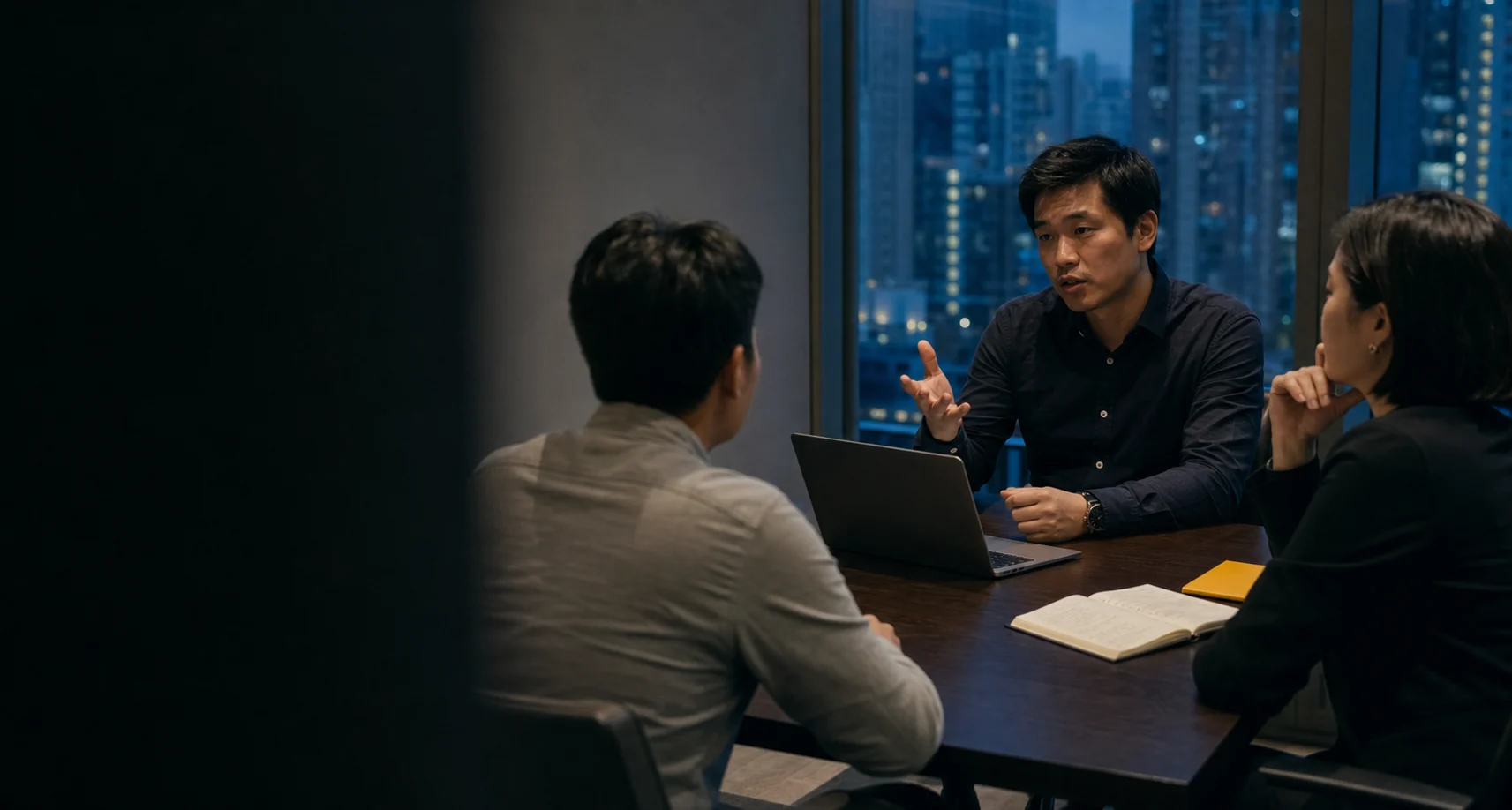Three colleagues holding a working meeting around a laptop and an open notebook.